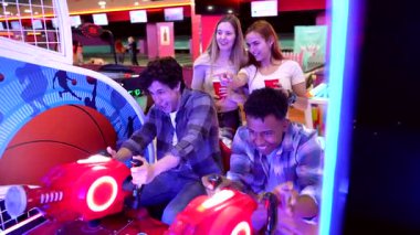 Motosiklet yarışı atari oyunu oynarken rekabetçi bir heyecan yaşayan genç yetişkinler, oyun etkileşimi ve arkadaşlığın neşeli anlarını paylaşıyorlar.