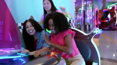 Çok oyunculu araba yarışı atari oyunu sırasında heyecanla yarışıp neşeli anları ve kahkahaları paylaşan bir grup genç arkadaş.