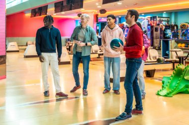 Çok ırklı arkadaşlar, günlük kıyafetler giyip bowling salonunda eğleniyorlar.