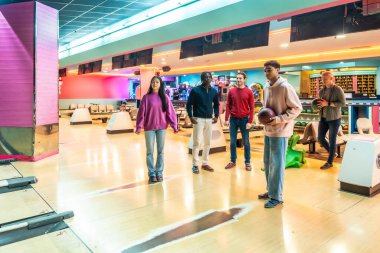 Bowling sahalarında dikilen, toplarını tutan, renkli bir bowling salonunda eğlenmeye hazır beş genç arkadaş