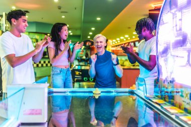 Çoklu etnik arkadaşlar hava hokeyi oynuyorlar, eğleniyorlar ve birlikte eğleniyorlar.