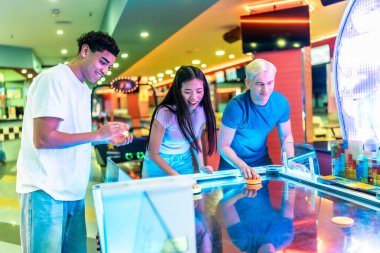 Genç çok ırklı arkadaşlar canlı bir eğlence merkezinde hokey oynuyorlar.