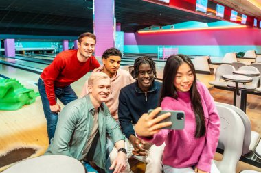 Bir grup çok ırklı genç arkadaş bowling salonunda selfie çekiyorlar, birlikte hafta sonunun tadını çıkarıyorlar.