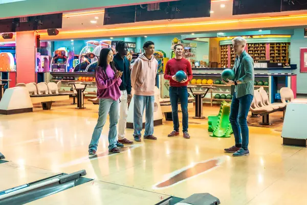 Parlak bir eğlence merkezinde çok ırklı arkadaşlar birlikte bowling oynuyorlar.