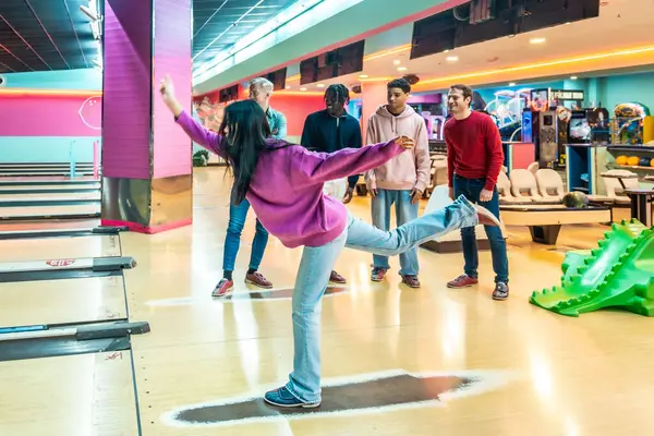 Genç bir kadın bovling oynarken arkadaşlar neşeli bir bowling salonunda coşkuyla tezahürat yapıyor, herkes için eğlenceli ve destekleyici bir ortam yaratıyor.