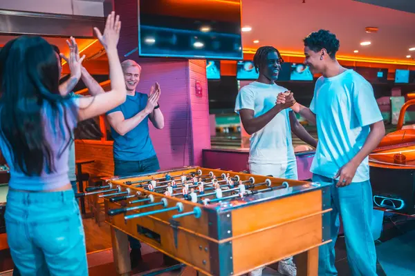 Çoklu etnik arkadaşlar langırt oynuyorlar, zaferlerini canlı bir bowling salonunda beşlik çakarak ve el sıkışarak kutluyorlar.