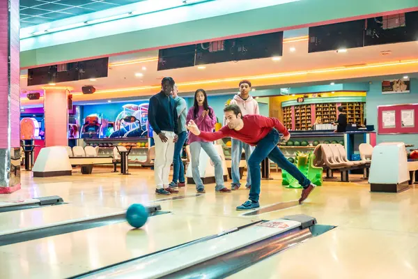 Bir grup çok ırklı arkadaş birlikte bowling oynuyor, hafta sonları aydınlık bir bowling salonunda eğleniyorlar.