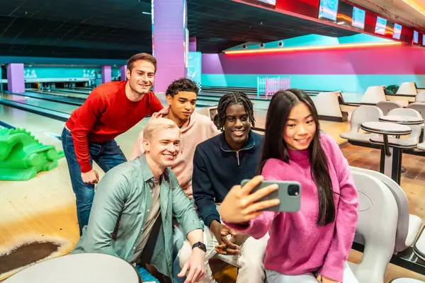 Bir grup çok ırklı genç arkadaş bowling salonunda selfie çekiyorlar, birlikte hafta sonunun tadını çıkarıyorlar.