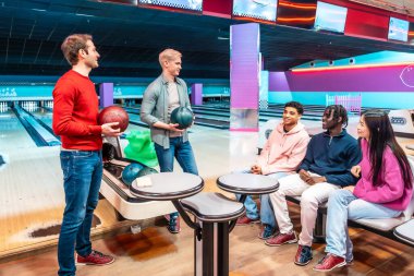 Çok ırklı bir grup genç arkadaş bowling salonunda eğleniyor ve bowling oynuyorlar.