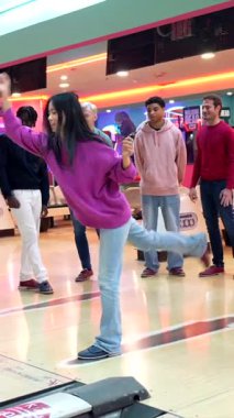 Genç bir kadın, destekleyici arkadaşlarıyla bovling oynuyor, arkadaşça bir rekabet ortamı yaratıyor ve eğlenceli aktivitelerden keyif alıyor.