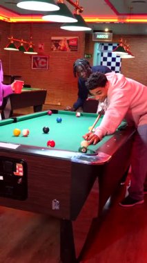 Genç arkadaşlar bilardo oynuyor, yetenek ve coşku sergiliyorlar ve zaferi canlandırılmış etkileşim ve günlük bar ortamında rekabetçi ruhla kutluyorlar.