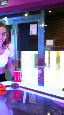 Enerjik bir hava hokeyi maçı oynayan rekabetçi genç çift, renkli ışıklandırmalı canlı oyun salonunda gülüyor ve eğleniyor.