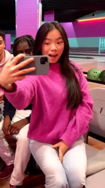 Çeşitli çok ırklı arkadaşların grup selfie 'sini çekmesi, akıllı telefonlarla bowling oynayıp gülmeleri ve eğlenmeleri renkli bovling salonlarında eğlenceli anları paylaşmaları.