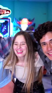 Çeşitli genç arkadaşlar neşeli anları paylaşıyor, renkli atari salonunda birlikte gülüyor ve oynuyorlar, tasasız oyun heyecanı yaşıyorlar.