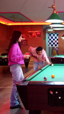 Genç yetişkinler canlı bilardo odasında sosyalleşiyor ve bilardo oynuyorlar, renkli neon ışıkları ve enerjik grup dinamikleriyle rekabetin tadını çıkarıyorlar.