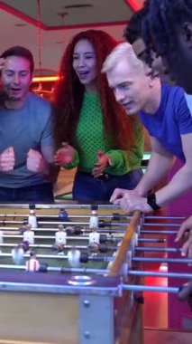 Arkadaşlar, canlı bovling salonunda oynanan masa futbolu maçında golü attıktan sonra enerjik bir şekilde kutlama yapıyor, rekabetçi oyun ve dostluk anlarını paylaşıyorlar.