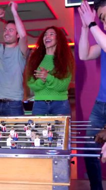 Çeşitli arkadaş grupları coşkulu eğlence kulübünde rekabetçi masa futbolu oynarken tezahürat yapıyor, beşlik çakıyor, zafer anlarını paylaşıyor.