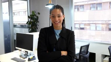 Kendine güvenen iş kadını kollarını kavuşturup modern ofis ortamında profesyonel başarı yayıyor.