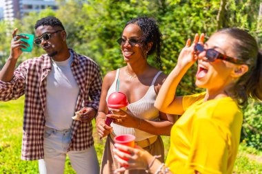 Üç arkadaş parkta birlikte eğleniyorlar güneşli bir günde içecek ve atıştırmalıkların tadını çıkarıyorlar.