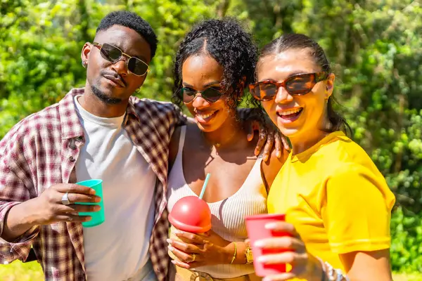 Üç neşeli arkadaş dışarıda eğleniyor güneşli bir yaz gününde ferahlatıcı içkilerin tadını çıkarıyorlar.