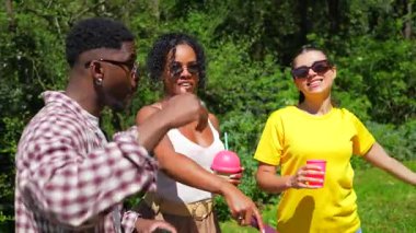 Genç arkadaşlar gülüyor, içiyor, güneşli bir öğleden sonra yeşil parkta eğleniyor, mutluluk ve bağlantı anlarını paylaşıyorlar.