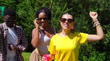 Genç arkadaşlar parkta eğleniyorlar, dans ediyorlar ve birlikte içeceklerin tadını çıkarıyorlar.