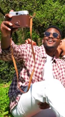 Genç arkadaşlar klasik fotoğraf makineleriyle selfie çekiyorlar ve parkta meyve ve cipslerle pikniğin tadını çıkarıyorlar.