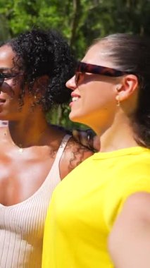 Neşeli arkadaşlar selfie anı yakalar, güneşli park gününün tadını çıkarırlar, gezici cihazlarla kahkaha ve arkadaşlığı paylaşırlar, dışarıda boş zamanı kucaklarlar.