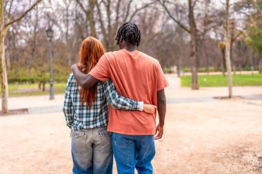 Genç, ırklar arası bir çift parkta birlikte yürüyor, doğanın güzelliğini kucaklarken birbirlerinin arkadaşlığından keyif alıyorlar.