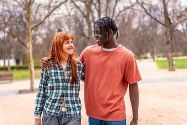 Parkta birlikte yürüyen iki genç yetişkin, neşeli bir anı paylaşıyorlar. Sahne, arkadaşlığı ve mutluluğu doğal bir ortamda yakalıyor.