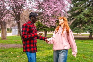 Irklar arası bir çift parkta bahar gününün tadını çıkarıyor, el ele tutuşuyor ve akıllı telefona bakıyor.