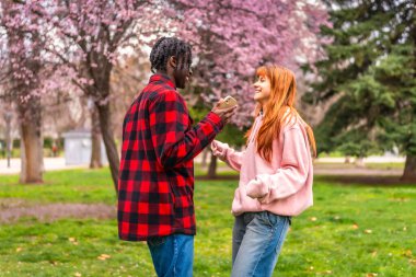 İki genç yetişkin, çiçek açan kiraz çiçeklerinin altında neşeli bir sohbete girişiyor, halka açık bir parkta canlı bir arkadaşlık ve doğa manzarası yaratıyorlar.