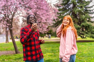 Genç, çok ırklı bir çift, canlı bir parkta, çiçek açan kiraz çiçekleriyle dolu, kahkaha ve mutluluğu paylaşan bir video çağrısının tadını çıkarıyor.