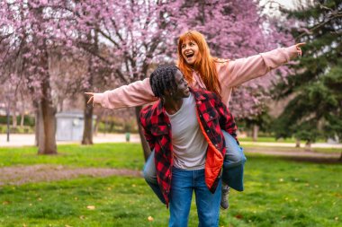 Mutlu ırklar arası çift baharda çiçek açan pembe ağaçlarla dolu bir parkta eğleniyor.