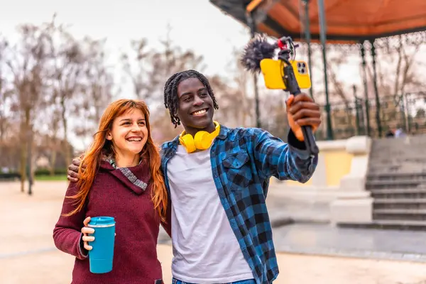 İki genç içerikli yaratıcı parktaki bir video blogunu mikrofonla kaydediyor.