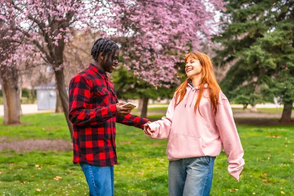 Irklar arası bir çift parkta bahar gününün tadını çıkarıyor, el ele tutuşuyor ve akıllı telefona bakıyor.