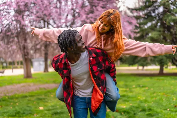 Genç adam, baharda kiraz çiçekleriyle dolu bir parkta kız arkadaşını sırtında taşıyor.