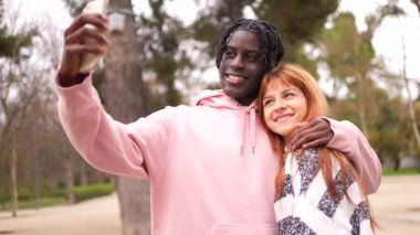Genç, çok ırklı bir çift unutulmaz selfie çekerken birlikte güzel vakit geçiriyorlar. Gülümsüyorlar ve manzaralı sonbahar parkında romantik anların tadını çıkarıyorlar. Doğayla iç içe.