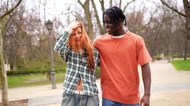 Bereketli parkta birlikte yürüyen çok ırklı çift, sıcak kucaklaşmayı paylaşıyor, güneşli açık havanın tadını çıkarırken neşe ve derin bağları ifade ediyorlar.