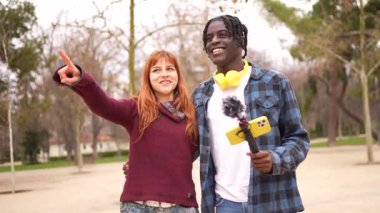 İki genç gazeteci, bir erkek ve bir kadın, bir video kaydı yaparken parkta yürüyorlar.