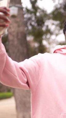 Çok ırklı genç bir çift parkta telefonlarıyla selfie çekiyor, sarılıyor ve gülümsüyor.