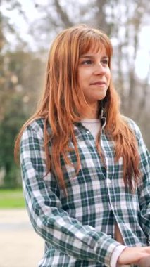 Kareli tişörtlü kızıl bir kadın parkta bankta otururken rahatça sohbet ediyor. Bağlantı anını ve anlayışını paylaşıyor.