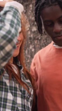 Gülümseyen çok ırklı bir çift, neşeli bir anı paylaşırken güneşli park ortamında akıllı telefon içeriğini izleyip gerçek bir bağ ve mutluluk sergiliyor.