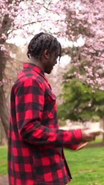 Gen z çifti parkta çiçek açan güzel bir kiraz ağacının altında akıllı telefonlarıyla komik mimler ve videolar paylaşıyor.