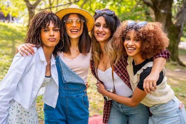 Dört farklı genç kadın birbirine sarılıyor, parkta kaygısız bir günün tadını çıkarıyor, birlik ve mutluluğu somutlaştırıyor.