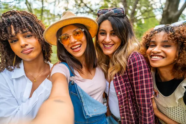 Parkta kucaklaşan ve selfie çeken dört neşeli genç kadın birlikte vakit geçiriyorlar.
