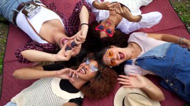 Kırmızı battaniyeyle bağlanan genç kadınlar, açık hava boş zamanlarında neşeli kalp hareketleri ve neşeli ifadeler yaratıyorlar, dostluk ve neşe sergiliyorlar.