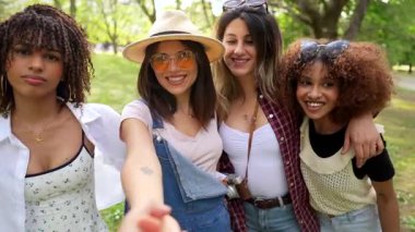 Canlı bir bahar gününün keyfini çıkarırken selfie çeken dört genç kadın yemyeşil bir parkta neşeli anlar paylaşıyorlar. Arkadaşlık ve kaygısız bir enerji yayıyorlar.