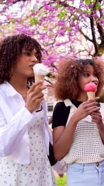 Arkadaşlar çiçek açan parkta toplanıyor, lezzetli dondurma külahlarını paylaşıyor, gülümsüyor ve birlikte canlı bahar gününün tadını çıkarıyorlar.
