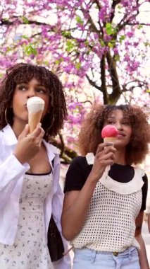 Üç genç kadın, bir bahar günü güzel ağaçların altında dondurma külahlarının tadını çıkarırlar.